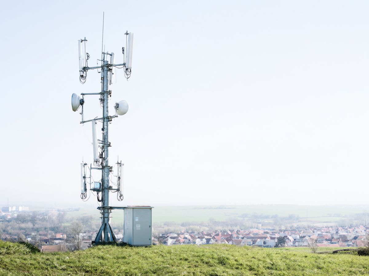 A rural wireless tower with sector antennas on a hill above a village with red roofs