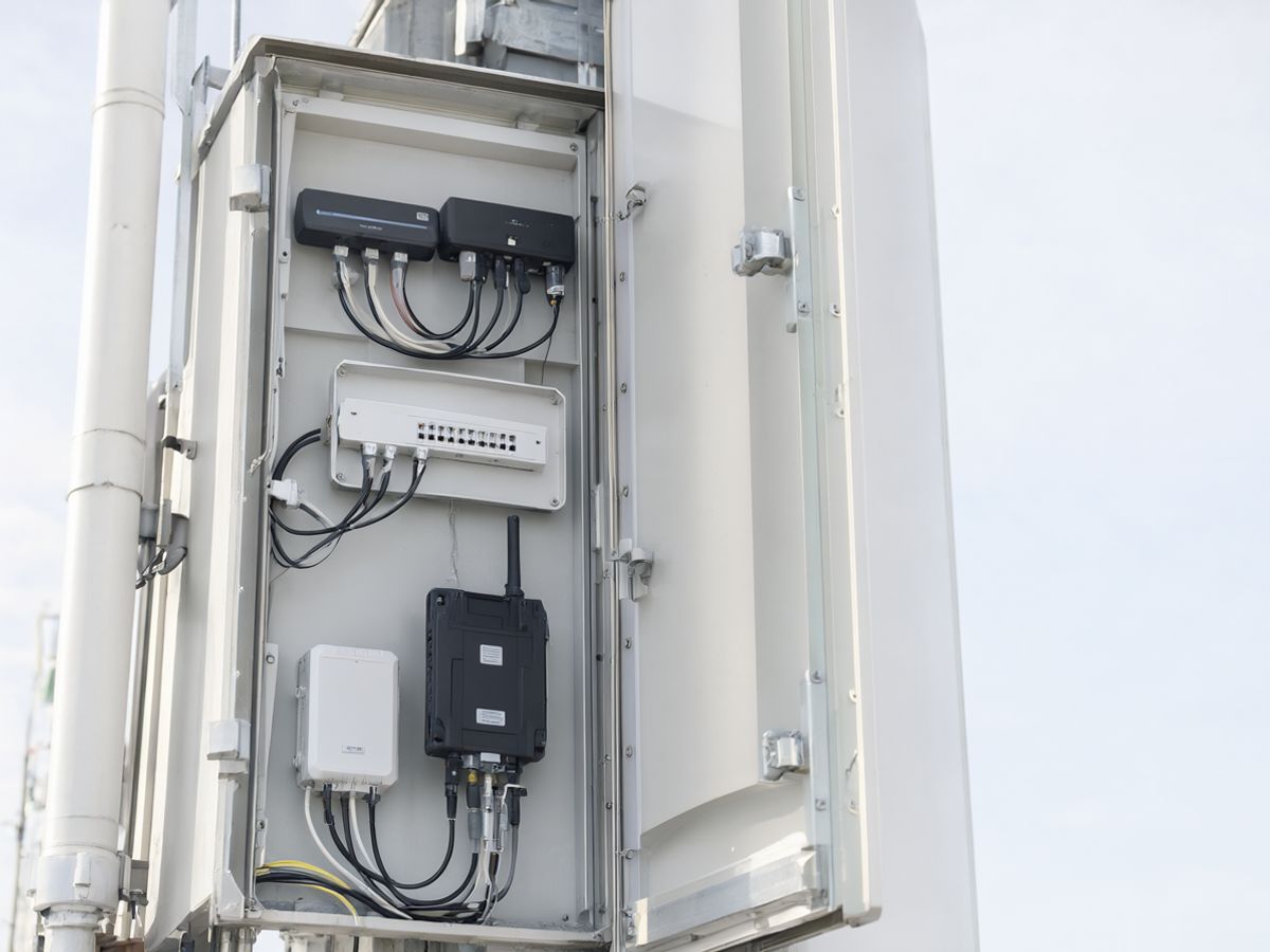 An open outdoor telecom cabinet at the base of a tower with routers
