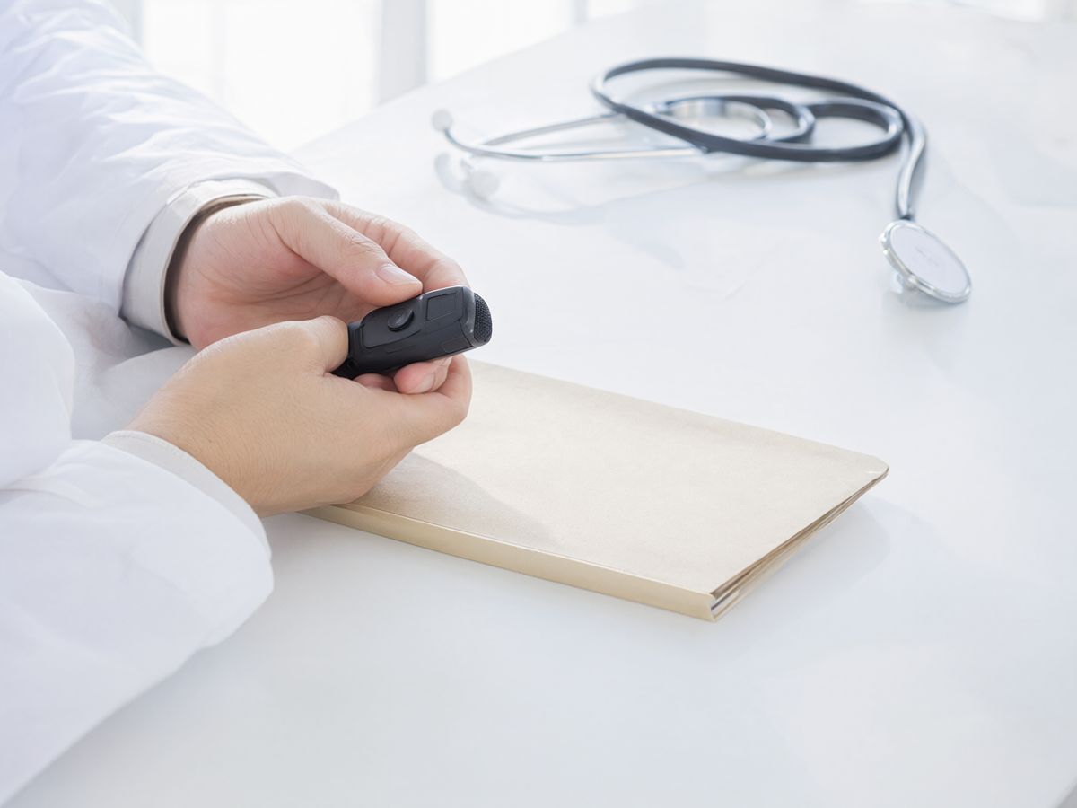 A doctor's hands in white coat sleeves holding a handheld dictation microphone above a patient folder