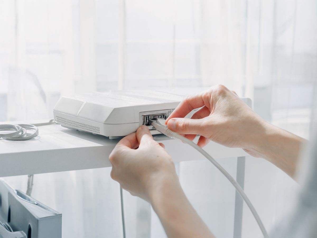 A technician's hands plugging a network cable into a small white router on an office shelf