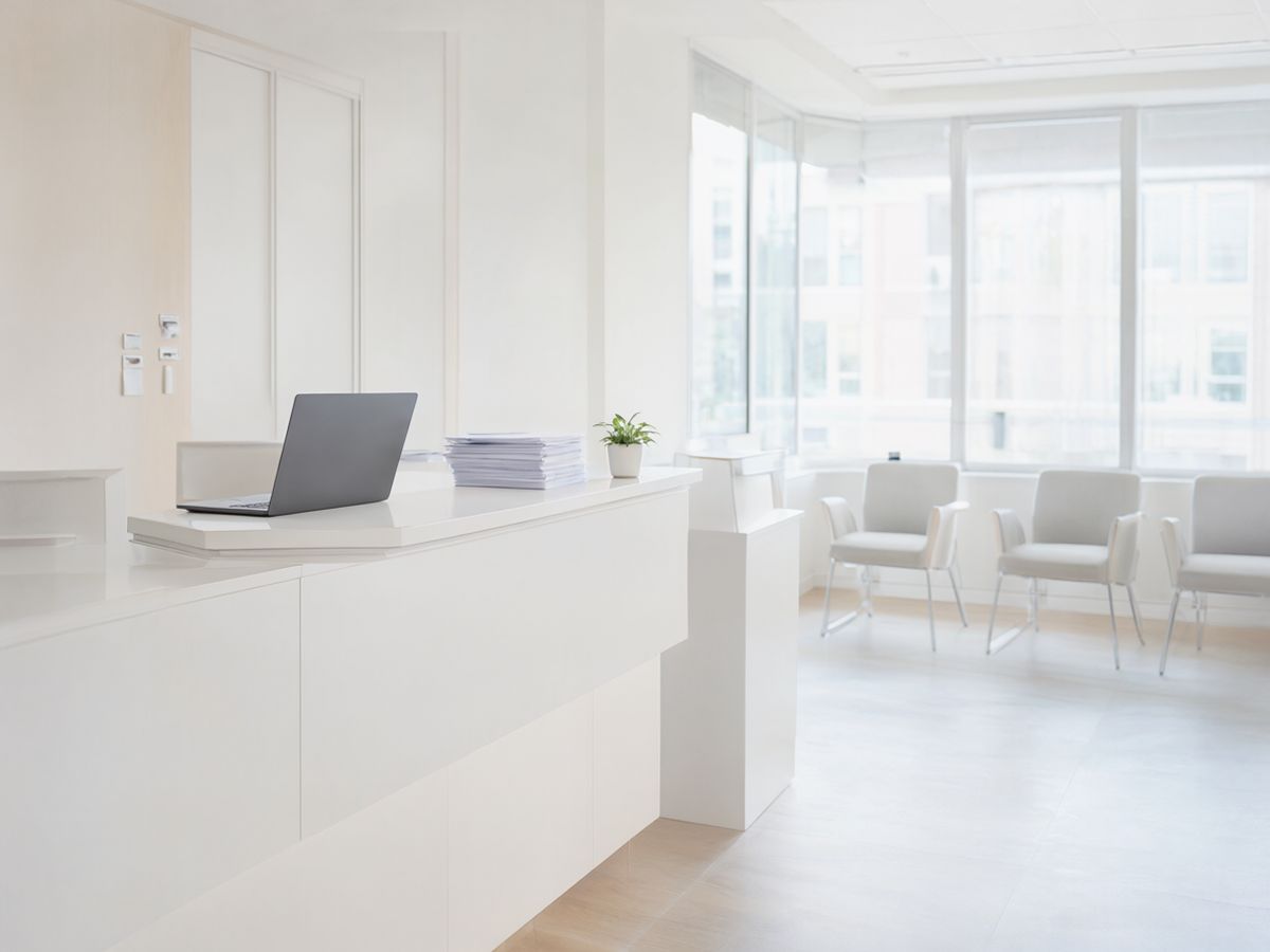 A bright private clinic reception with a white counter and a waiting area