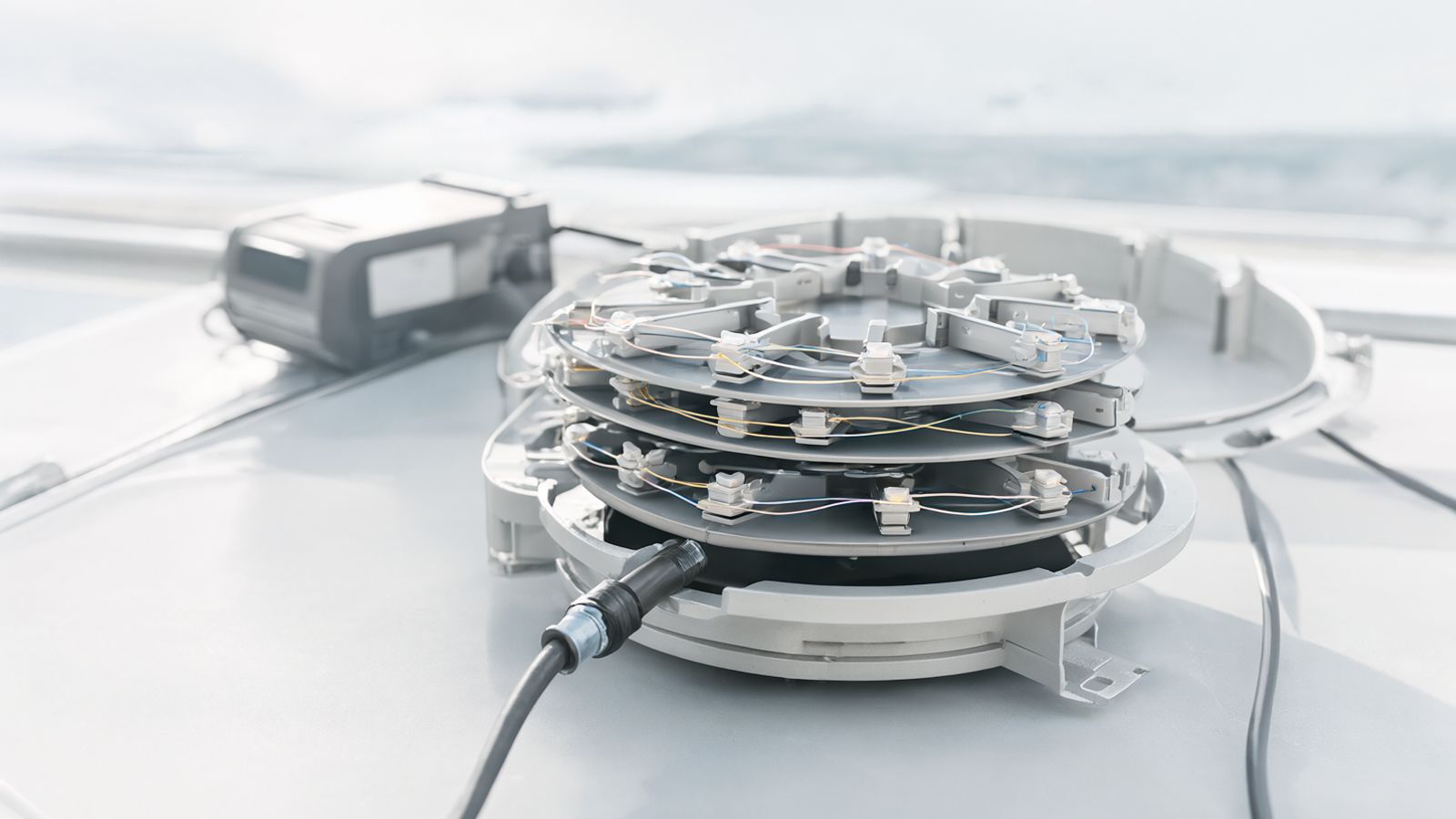 An open outdoor fibre splice closure with its trays fanned out, coloured fibres looped around the trays and protection sleeves on the splices