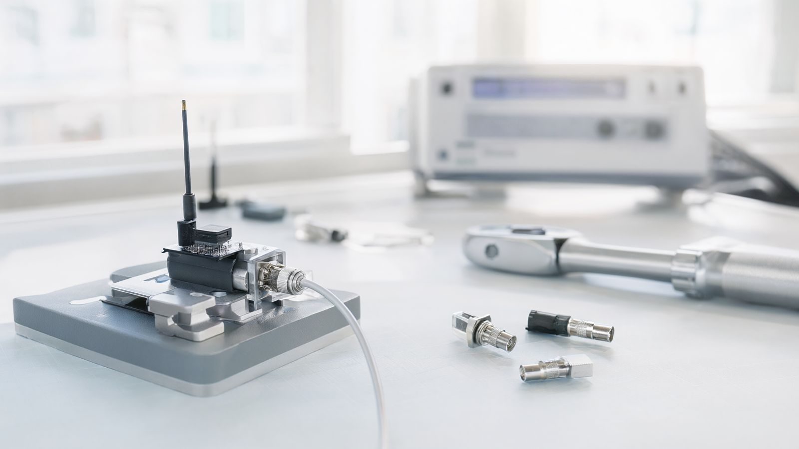An IoT circuit board with a small antenna in a test fixture, connected by a coaxial cable with an SMA connector to a test port